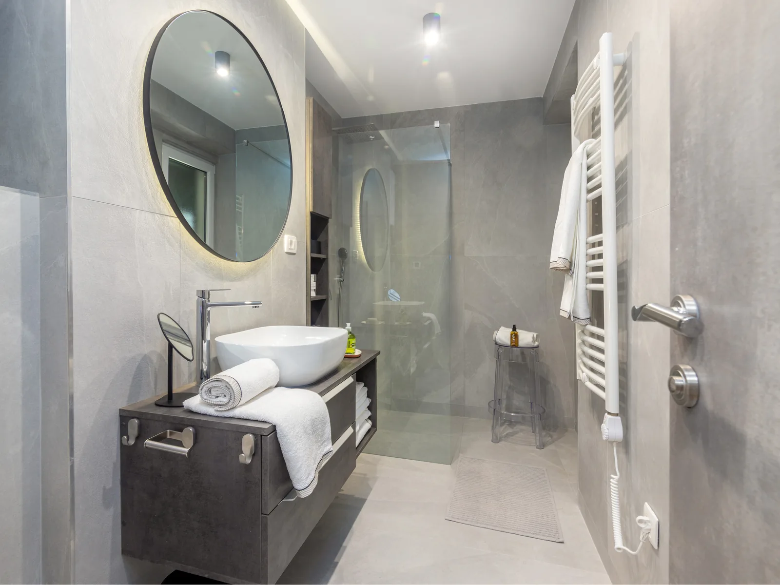 Bathroom with walk-in shower, round mirror and towel warmer