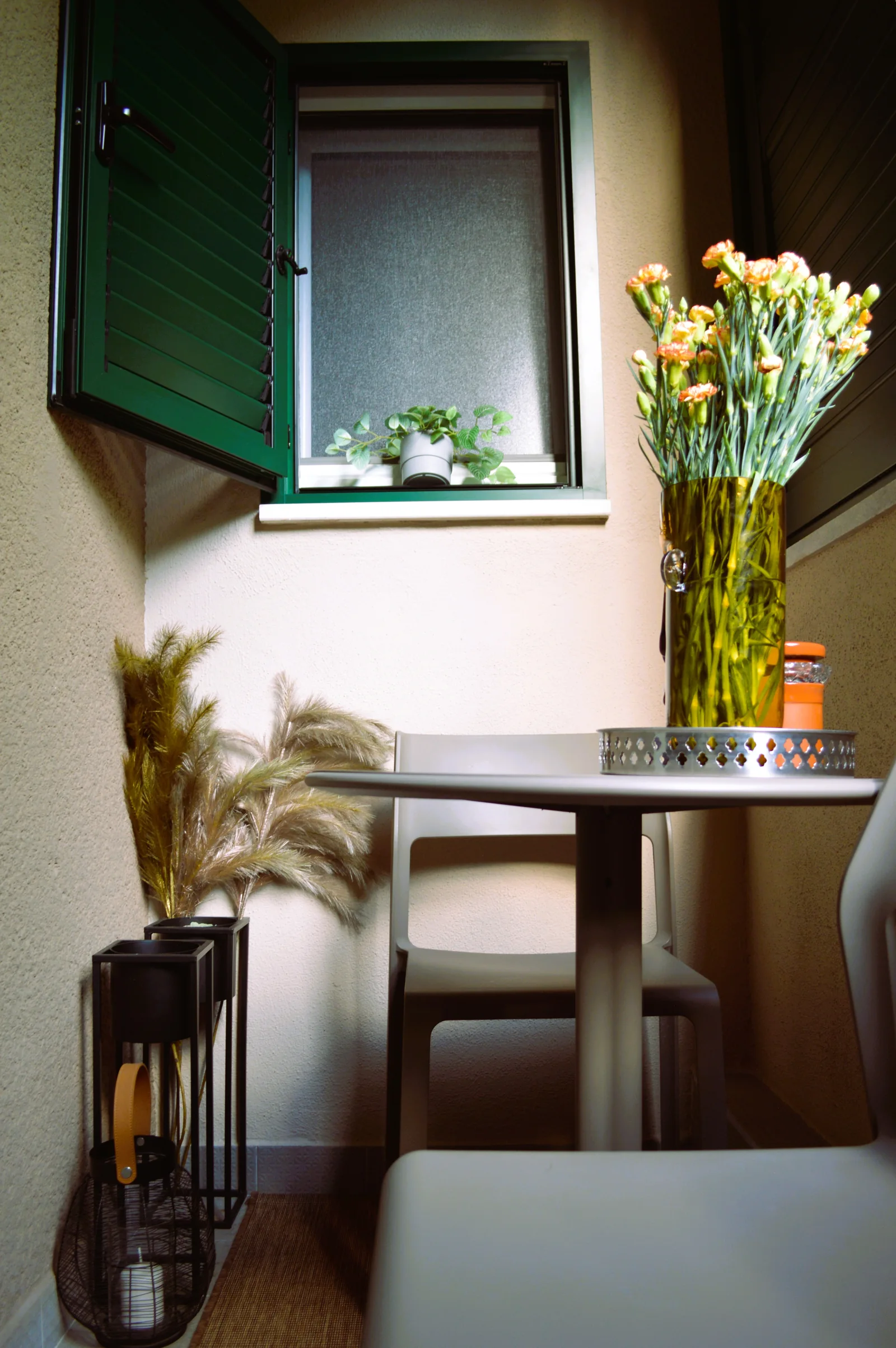 Balcony with a small table, chairs and flowers beside green shutters